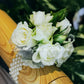 A wrist corsage featuring white flowers and green leaves for school formal, attached to a clear band.