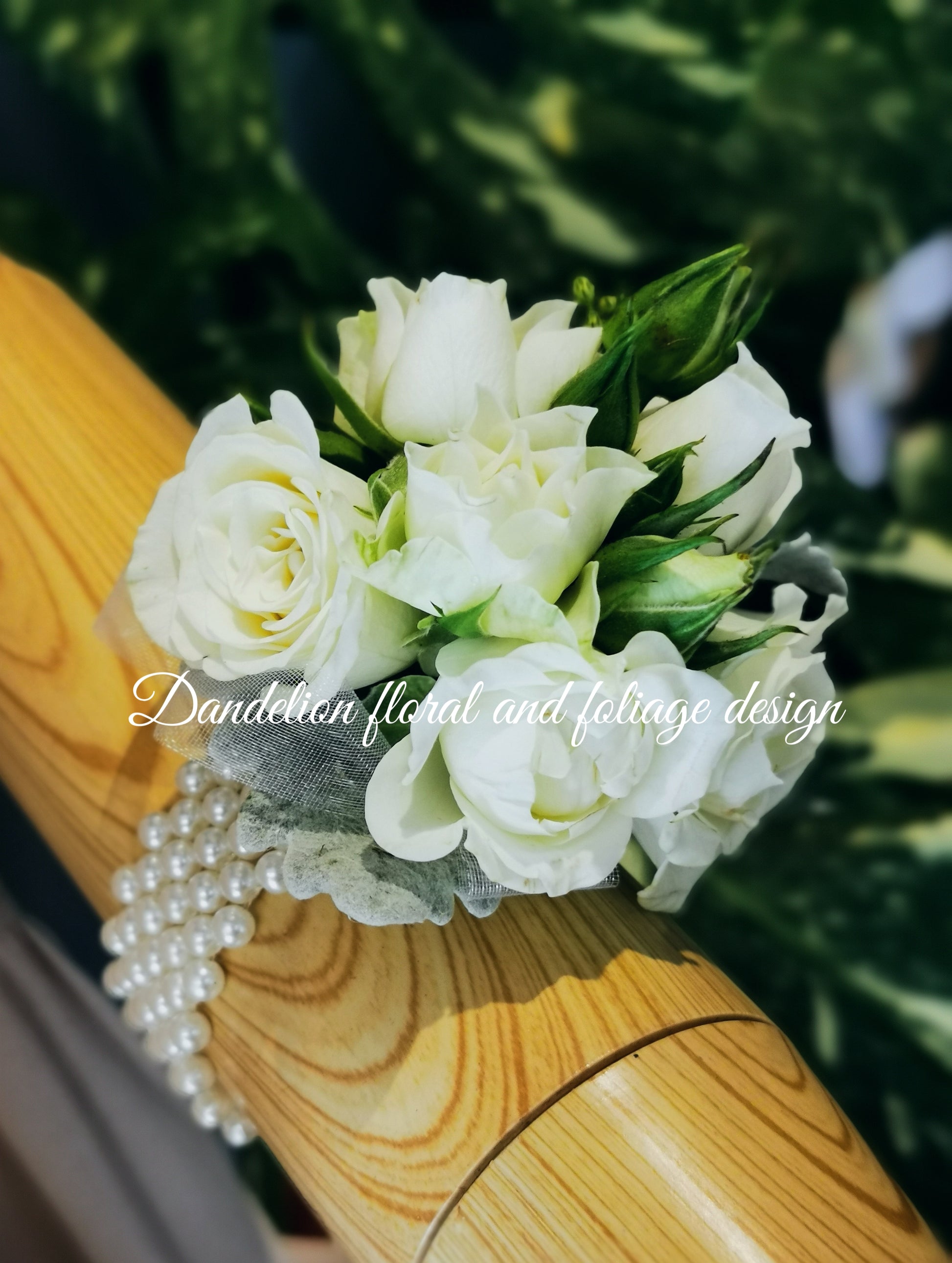 A wrist corsage featuring white flowers and green leaves for school formal, attached to a clear band.