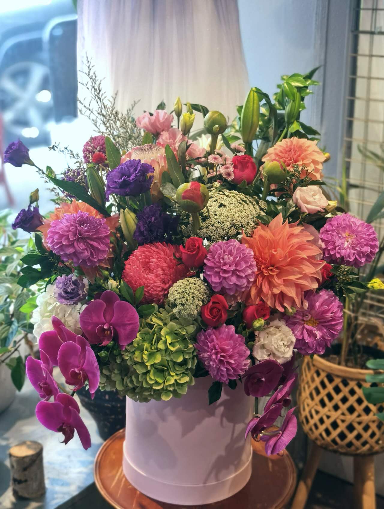 A floral arrangement featuring a variety of flowers including pink roses, orchids, and other plants in a hat box. Whether you're celebrating birthdays, anniversaries, weddings, or extending sympathy and support, our flowers and gifts are crafted to resonate with the unique emotions of each moment. Our commitment to quality ensures that every floral arrangement and gift is an embodiment of your care and consideration, destined to leave an impression.