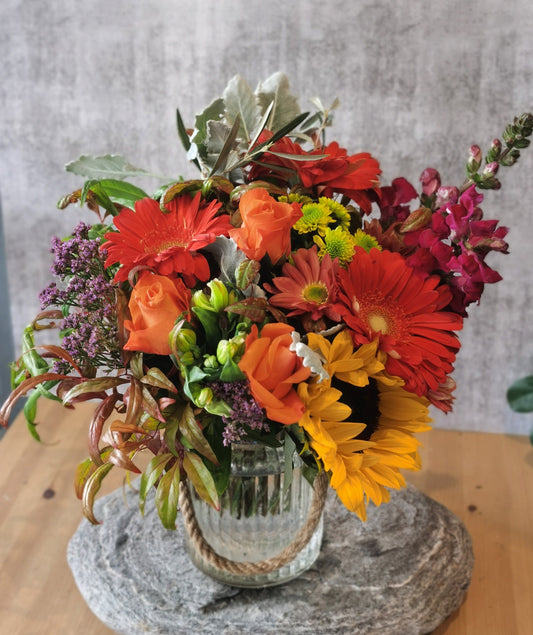 This fun bunch of flowers features sunflowers, gerberas, chrysanthemums and snapdragons. Ideal for all occasions. It comes with a hurricane vase as pictured.