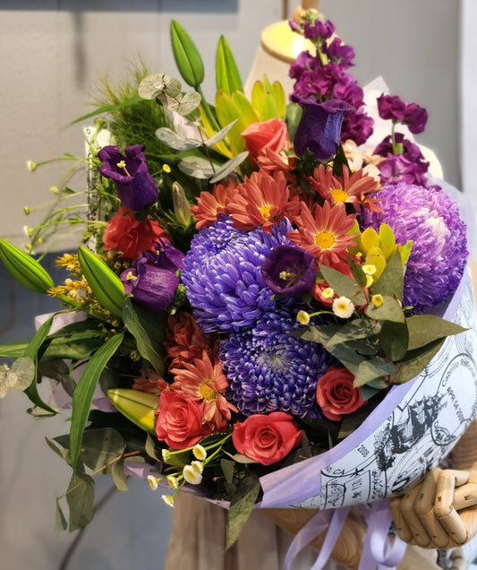 Bursting with colour and variety, this fun bunch of flowers features lilies, roses, Canterbury bells, chrysanthemums and stocks.