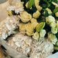 A stunning floral arrangement featuring a mix of white roses, lilies and other seasonal fresh flowers with accompanying green foliage. 
