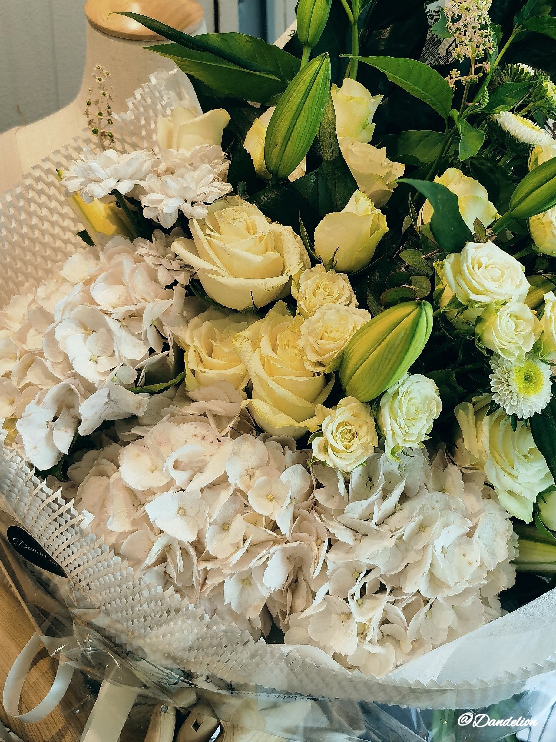 A stunning floral arrangement featuring a mix of white roses, lilies and other seasonal fresh flowers with accompanying green foliage. 