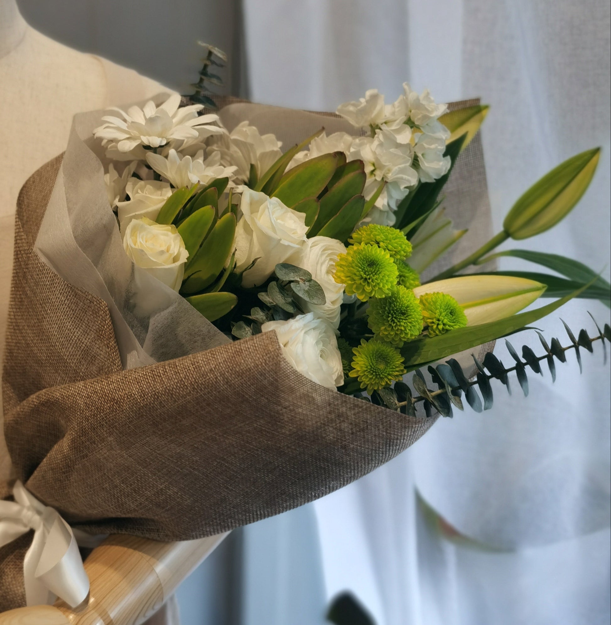 A bouquet of white and green flowers wrapped in brown paper. 